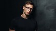 © Ivan - A muscular man stands confidently against a textured dark background, wearing glasses and a fitted black shirt. His expression is serious, adding to the dramatic atmosphere