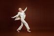 © deagreez - Successful mature businesswoman wearing an elegant white suit poses stylishly against a minimalist brown background