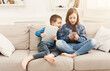© Prostock-studio - Two kids with gadgets. Sister and brother sharing funny content on smartphone and digital tablet on sofa at home. Family friendship and communication concept