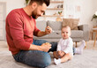 © Prostock-studio - Cute Young Dad Spoon Feeding Little Baby Toddler Caring For Daughter During Paternity Leave Sitting On Floor At Home. Healthy Nutrition For Newborn, Fatherhood And Child Care Concept