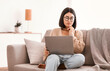 © Prostock-studio - Pensive asian female freelancer in glasses with laptop brainstorming at new project, making research in internet, having remote job, sitting on couch in living room at home, looking at computer screen