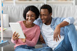 © Prostock-studio - Smiling black lovers with digital tablet sitting on floor in living room, having idea to clean apartment, closeup. Happy african american young man and woman looking for house-keeping service