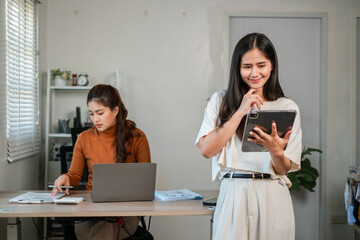 Wall Mural - two women in a modern office setting, one using a laptop and the other a tablet, engaged in work and