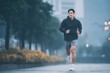 © SITI - Fit Young Man Jogging Outdoors on Urban Street in Early Morning Mist Wearing Sportswear and Hoodie
