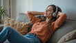 © Ornpitchayawee - Young woman relaxing on a cozy couch with headphones, enjoying music in a bright and comfortable living room space