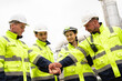 © winnievinzence - Team of refinery engineers joining hands together in front of an oil refinery, symbolizing teamwork, unity, and collaboration in the industrial energy sector. Wearing safety gear and protective clothi
