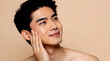 © Victoria - Attractive young man, Asian appearance, with glowing skin, gently touching his face, on a beige background.