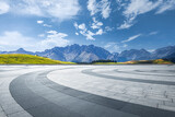 Empty curved stone floor offering a panoramic view of green hills and majestic mountains under a blue sky.