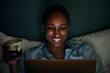 © Maskot - Smiling woman holding mug while using laptop in bedroom at night