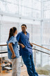 © Maskot - Male healthcare professional leaning on railing while talking with female coworker in hospital corridor