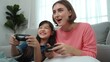 © InfiniteFlow - Caucasian mom and daughter sitting and playing game at living room. Happy mother spend time together with smart asian girl while holding joystick ans enjoy playing games. Lifestyle concept. Pedagogy.