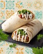 © MarinkaLev - shawarma wrap with parsley and sauce, placed over patterned background with mosaic motifs, graphic street food layout