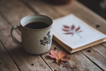 Poster - Warm Mug of Coffee Beside Vintage Notebook With Falling Leaf Sketch on Rustic Wooden Table Generative AI