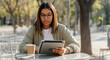 © Postmodern Studio - Young hispanic female using tablet in outdoor cafe with coffee on table