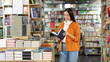 © Home-stock - Young woman buying books at bookstore and reading one while choosing best seller, bookshelves on background