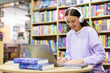 © Home-stock - Happy engaged female student watching webinar, attending online class and writing, studying in library with headphones, laptop, books