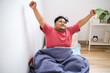© Gatot - Asian Fat Man Waking Up in The Morning Sitting on Bed and Stretching