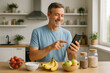 © Verda Vista - Happy man uses phone app planning healthy meal fruit banana strawberry apple kitchen