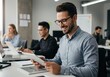 © Vooglo - Smiling man using a tablet in a modern office setting with colleagues working in the background