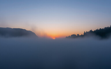Poster - Serene sunset over a misty landscape.  The sun dips below the horizon, its warm light illuminating the fog-shrouded hills. A tranquil and peaceful scene.