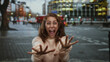 © Krakenimages.com - Woman in sweater outdoors on city street showing excitement with buildings and traffic in the background during daytime.
