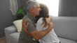 © Krakenimages.com - Middle-aged couple embracing lovingly in a cozy living room, conveying warmth and affection, surrounded by homely decor and natural light.