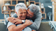 © peopleimages.com - Laughing, hug and senior couple in home, retirement and commitment to relationship, love and living room. House, old man and embrace for woman in lounge, pensioner and happy for romance on couch