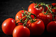 © Jossfoto - Primer plano de tomates rojos frescos en rama con gotas de agua brillantes, sobre superficie oscura.