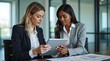 © Nathan - Two professional women engaged in a discussion over a tablet in a modern office setting.