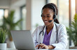 © Maryna - Smiling African American doctor with headset consults patient online using laptop at hospital. Telemedicine, telehealth, online healthcare service concept. Remote medical assistance, virtual patient