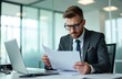 © Maryna - Serious businessman reviews papers, contracts in office. Executive wears glasses, business suit, works with laptop. Concentrated employee, reads documents at desk. Financial manager analyzes reports.