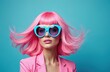 © Maryna - Attractive woman wearing vibrant pink wig, blue sunglasses on blue background. Fashion portrait of stylish girl, fun make-up. Modern beauty, trendy model with colorful coiffure, bright style.