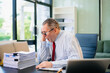 © laddawan - Senior businessman rips paperwork in rage at office desk. Workplace stress, anger, chaos, and burnout concept with files