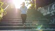 © justholla - A person jogs up a sunlit staircase, surrounded by greenery, embodying fitness and determination in a serene outdoor setting