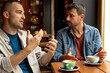 © we.bond.creations - Two men sitting together at a table in a cafe, enjoying coffee and engaging in animated gestures while discussing various topics