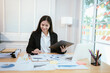 © Natthawadee - A young Asian businesswoman sits at her office desk with a laptop, focused and thinking, analyzing data for a corporate project.