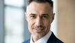 © NAPHAT - Confident Businessman in Suit Smiling at Camera with Modern Office Background and Bright Natural Light