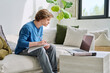 © Valerii Honcharuk - Teenager guy student studying sitting at home on sofa using laptop textbook notebook