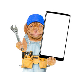 Poster - Funny Mastiff puppy wearing blue cap and denim overalls with tool belt showing big smartphone with white blank screen in it paw. Isolated on white background