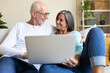© Daniel - Happy mature married couple in love using laptop relaxing on the couch at home living room looking at each other.