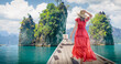© Vladimir Razgulyaev - A famous cliffs and islands of Thailand to advertise tours. A woman in a dress on a Thai longtail boat looks at the Three Rocks nature panorama on Cheo Lan Lake in Khao Sok Park.