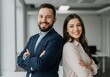 © Rehena - Smiling man and woman stand back to back with arms crossed in modern office