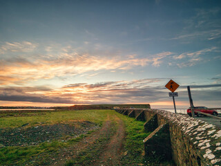 Wall Mural - Peaceful sunrise nature scene with green field, stone fence and car track on the ground and spectacular and dramatic sky. Galway city area, Ireland. Irish landscape scene. Nobody. Travel and tourism.