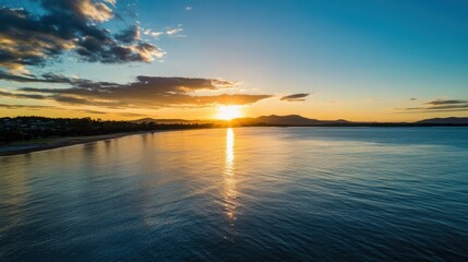 Leinwandbilder - Serene sunset over calm ocean waters, reflecting golden light on the tranquil surface, with a distant coastline and mountains silhouetted against the vibrant sky. : Generative AI