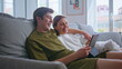 © stockbusters - Embracing lovers using tablet laughing at home closeup. Positive couple cuddling