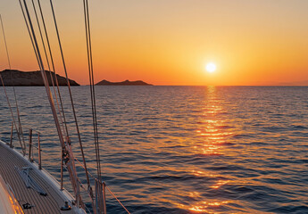 Fototapete - Golden sunset over the Aegean sea, viewed from a sailboat's deck, with islands on the horizon.  Warm light reflects on the water's surface. : Generative AI