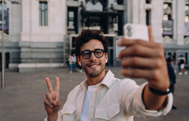 stylish influencer captures selfie with historic landmark in the background. His relaxed expression and peace sign reflect a fun and engaging social media moment, sharing his adventures with followers