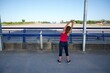 © cjsolanop - Young active woman in sportswear stretching her arms outdoors by blue metal railings under a clear sky. Concept of healthy lifestyle, fitness, morning exercise, and outdoor activity