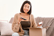 © Prostock-studio - Product Review. Portrait of cheerful asian woman received present beauty box with cosmetics, holding eyeshadow palette for makeup, unpacking cardboard parcel, sitting on the sofa at home