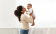 © Prostock-studio - Mom's Love. Young Black Mother Holding Baby Toddler Playing And Cuddling With Little Infant Son Standing Near Window Indoor. Motherhood Happiness And Child Care, Maternity Leave Lifestyle. Side View
